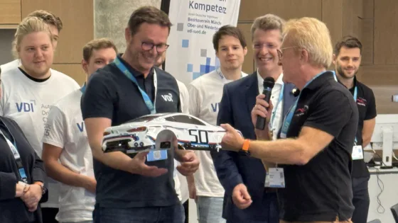 Zu sehen ist Alexander Bloch bei der VDI Autonomous Driving Challenge 2025, powered by MdynamiX. Ihm wird von Markus Krug die Karosserie des BMW 3.0 CSL Hommage R übergeben