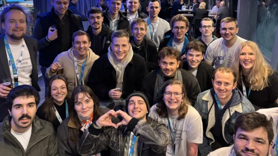 Gruppenfoto von Teilnehmenden der VDI Autonomous Driving Challenge 2025, powered by MdynamiX, aufgenommen auf dem Eventschiff „MS RheinMagie“. Die Personen tragen überwiegend Event-Lanyards und teilweise T-Shirts mit VDI-Logo und Challenge-Aufdruck. Im Vordergrund formt eine Person mit den Händen ein Herzsymbol. Im Hintergrund sind weitere Gäste an Tischen in einer modernen, stimmungsvoll beleuchteten Location zu sehen.