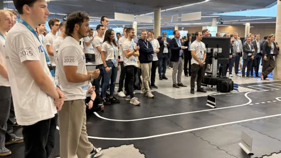 Teilnehmende und Gäste bei der VDI Autonomous Driving Challenge 2025, powered by MdynamiX, versammeln sich an einer markierten Teststrecke. Das Foto zeigt den Beginn der Siegerehrung moderiert von Alexander Bloch.