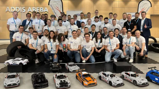 Gruppenfoto bei der Siegerehrung der VDI Autonomous Driving Challenge 2025, powered by MdynamiX. Eine große Gruppe von Teilnehmenden steht in mehreren Reihen vor einer Präsentationsfläche mit VDI-Bannern und Reifenstapeln. Im Vordergrund sind mehrere detailreiche Modellfahrzeuge in verschiedenen Farben und Designs aufgereiht.