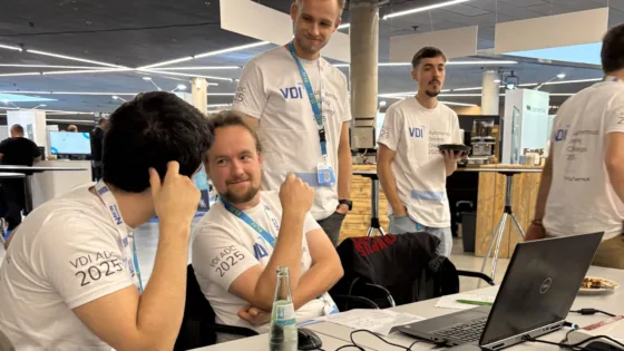 Das Foto zeigt das Team HS Bochum bei der VDI Autonomous Driving Challenge 2025, powered by MdynamiX. Mehrere Teilnehmende sitze in weißen Event-T-Shirts mit der Aufschrift „VDI ADC 2025“ an einem Tisch mit geöffnetem Laptop.