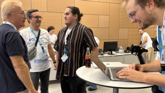 Zu sehen sind Teilnehmende der TU Berlin bei der VDI Autonomous Driving Challenge 2025, powered by MdynamiX. Im Vordergrund arbeitet eine Person an einem Laptop auf einem runden Stehtisch. Im Hintergrund stehen mehrere Personen in Gesprächsgruppen, einige tragen Event-T-Shirts mit der Aufschrift „VDI Autonomous Driving Challenge 2025“. 