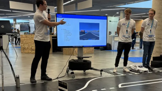 Präsentation bei der VDI Autonomous Driving Challenge 2025, powered by MdynamiX. Eine Person steht vor einem großen Bildschirm und erklärt Inhalte zum Thema „Vision“. Auf dem Bildschirm sind eine Überschrift „Vision“, eine Liste mit Punkten wie „Camera“, „Object Detection“, „Lane Detection“, „Traffic Sign Recognition“ sowie ein Bild einer Straße mit Fahrbahnmarkierungen und Verkehrsschildern zu sehen. 