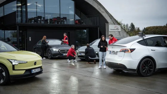 Gesamtflotte der Fahrzeuge, die dem Benchmark unterzogen werden, vor dem Shelter16, dem Hauptsitz von MdynamiX. Testingenieure von MdynamiX, dem IFM und auto motor und sport stehen um die Fahrzeuge und besprechen die finalen Testabläufe.