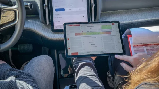 Testfahrer bewertet ein gefahrenes Fahrmanöver im ADAS-Benchmark mit der MXevalApp auf einem Tablet, das ihm von einer Mitinsassin überreicht wird.