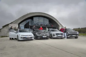 Gesamtflotte der Fahrzeuge, die dem Benchmark unterzogen werden, vor dem Shelter16, dem Hauptsitz von MdynamiX. Testingenieure von MdynamiX, dem IFM und auto motor und sport stehen um die Fahrzeuge und besprechen die finalen Testabläufe.