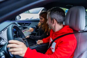 Expertin bespricht im Fahrzeug mit Fahrer die Bewertung einer Fahrzeugfunktion auf einem Tablet zur Ableitung von UX-Anforderungen und messbaren KPIs.