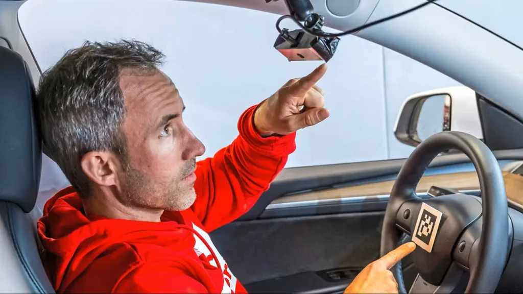 Techniker im Fahrzeug mit an der Sonnenblende montierter Kamera und codiertem Referenzmarker auf dem Lenkrad zur optischen Erfassung der Lenkradbewegung mit MXoptiCal.